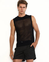 A male model wears a black Miami knit tank top and black shorts against a white background, posing with one hand in his pocket.