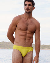 A man standing by the water wearing 2EROS neon yellow V10 core bikini swimwear.