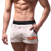 Beige cotton athletic shorts with black elastic waistband and side trim featuring orange logo patch on lower right leg