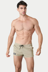 Shirtless male model wearing sand-colored AWRY hybrid swim shorts with a black drawstring and logo tag on plain background.