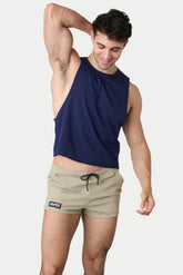A man wearing a navy blue AWRY Raw Crop Tank and beige shorts with one arm raised against a plain background.