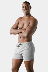 Shirtless male model wearing AWRY Menswear grey gym shorts with black drawstrings, standing with arms crossed.
