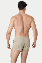 Back view of a shirtless man wearing AWRY Menswear sand-colored hybrid swim shorts against a white background.