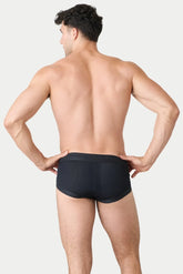 Rear view of a man wearing AWRY black Lift Brief underwear with a perforated pattern against a plain background.