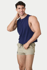 A model wears a navy blue AWRY Menswear Raw Crop Tank and beige athletic shorts while posing.