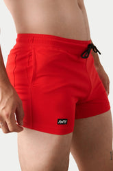 A man wearing bright red AWRY gym shorts with a black drawstring and small logo patch on the hem.