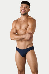 A smiling man posing in AWRY Menswear navy blue Oaisis classic swim brief against a plain white background.