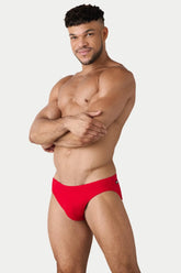 A muscular man wearing AWRY Menswear red Oasis classic swim briefs against a white background.