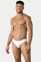 Smiling man wearing AWRY Menswear Oasis Classic white swim brief against a light gray background.