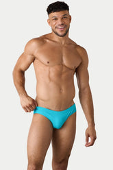 A smiling male model wearing AWRY Menswear cyan classic swim briefs against a white background.