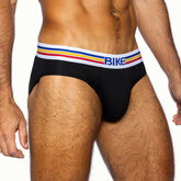 A man wearing BIKE Athletic black cotton brief underwear with a white, blue, yellow, and red striped waistband.