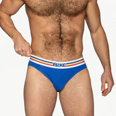 A muscular man wearing royal blue BIKE athletic cotton briefs with a white, red, yellow, and blue striped waistband.