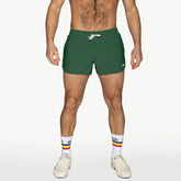 A man modeling green BIKE Athletic track shorts with a white drawstring waist, white socks, and sneakers.