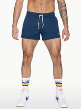 A model wears navy BIKE Athletic track shorts with a white drawstring, striped tube socks, and sneakers.