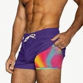 A shirtless man wearing purple gym shorts with a multicolored tie-dye liner and white drawstring.