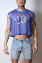 A man wearing a blue mesh crop top with the number 13 on the chest, paired with light wash denim shorts.