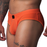 Bright orange textured mesh athletic brief with a wide waistband and a small black rectangular logo patch in front.