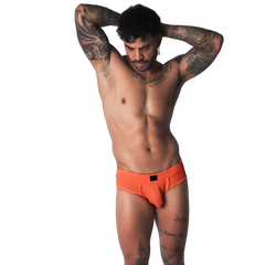 Bright orange low-rise brief in a textured, breathable fabric with a small black center-front logo patch.