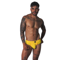 Yellow textured fabric jockstrap with a central black tab detail on the waistband, worn by a tattooed man.