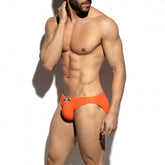 Athletic man wearing orange terrycloth swim bikini briefs with blue drawstrings, posing against a white background.