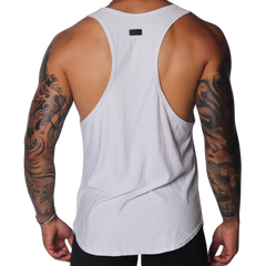 White racerback tank top with deep-cut sides, a curved hem, and a small black logo patch at the upper back.