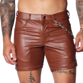 Brown faux leather fitted shorts featuring a button fly, belt loops, and a detachable silver chain detail at the hip.