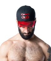 A bearded, shirtless man wears a black Nasty Pig baseball cap with a red translucent visor and matching red front logo.