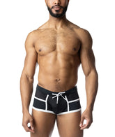 A shirtless man wearing black square cut swimwear with white trim and a drawstring against a white background.