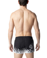Rear view of a man wearing Nasty Pig black and white oxidize swim trunks against a white background.