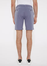 A pair of solid stretch knit shorts in soft lavender with lightweight fabric and dark button accents on back pockets backside view