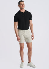 A model stands wearing white chalk-stripe jacquard knit chino shorts, a black polo, and white sneakers against a light background.