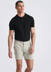 A man wearing vanilla-colored chalk stripe jacquard stretch knit chino shorts and a black polo shirt.