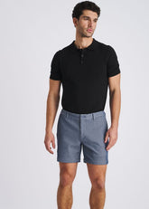 Male model wearing sky blue pinstripe stretch knit chino shorts and a black polo shirt against a white backdrop.