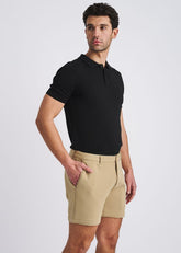 A man wearing khaki stretch knit chino shorts and a black polo shirt, posing against a white background.