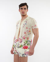 A man wearing a cream printed short-sleeved woven modal border shirt with floral and butterfly designs