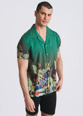 Male model wearing a POSTMARC emerald green short-sleeve button-down shirt with a multi-colored fauna border print.