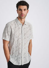 A man wearing a POSTMARC powder blue floral jacquard short-sleeve button-down shirt against a light background.