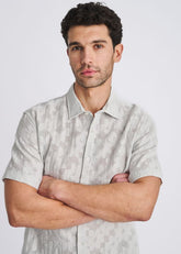 A man wearing a POSTMARC powder short-sleeve button-down shirt with a floral jacquard pattern, arms crossed.