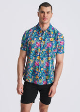 A man wearing a cobalt blue short-sleeve button-down shirt with a vibrant multi-color floral print and black shorts.