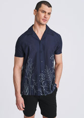 A male model wears a navy short-sleeve button-down shirt with white embroidered botanical borders along the hem.