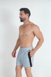 A man wearing grey fleece shorts with black and white side panels and a drawstring waist, standing against a white wall.