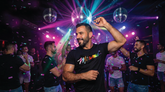 Man dancing in a crowded nightclub wearing a black Miami Pride T-shirt with a rainbow graphic logo.