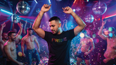 A man wearing a black t-shirt with multicolored Pride text dances in a nightclub with disco balls.