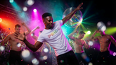 A man dances in a nightclub wearing a white Rico Starr t-shirt with rainbow Pride lettering.