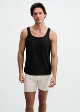 A male model wearing a black stretch ripped knit tank top and light-colored shorts against a white background.
