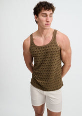A model poses in an olive green ST33LE stretch ripped knit tank top and white shorts against a white backdrop.