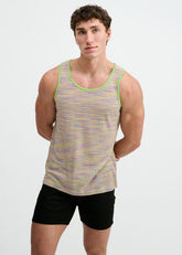 A man wearing a green, purple, and yellow space-dye textured knit tank top and black shorts, standing against a white wall.