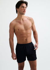 Shirtless male model wearing dark midnight gym shorts, standing against a plain white studio background.