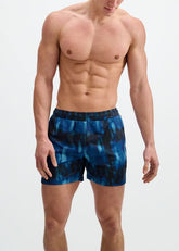 An athletic man wearing blue and navy abstract print mesh gym shorts against a white background.