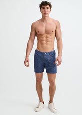 A shirtless male model wearing ST33LE powder blue floral jacquard stretch knit shorts and white sneakers.